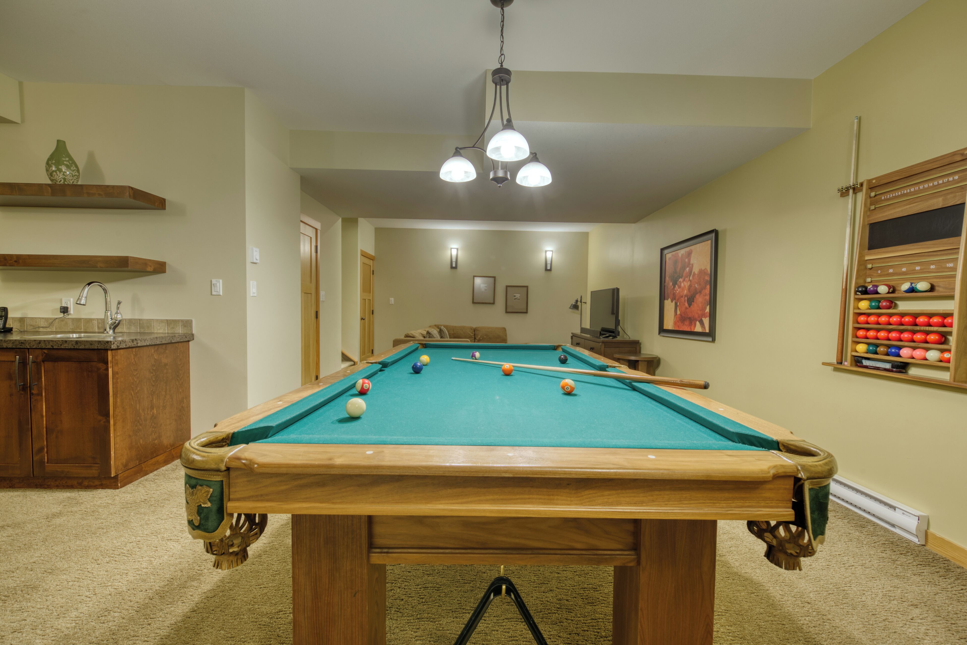 Una mesa de billar en una habitación con una zona de cocina, un estante de madera y un soporte para billares.