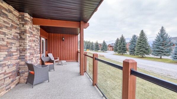 A covered outdoor area with wicker furniture, a stone wall, and a view of a road and trees.