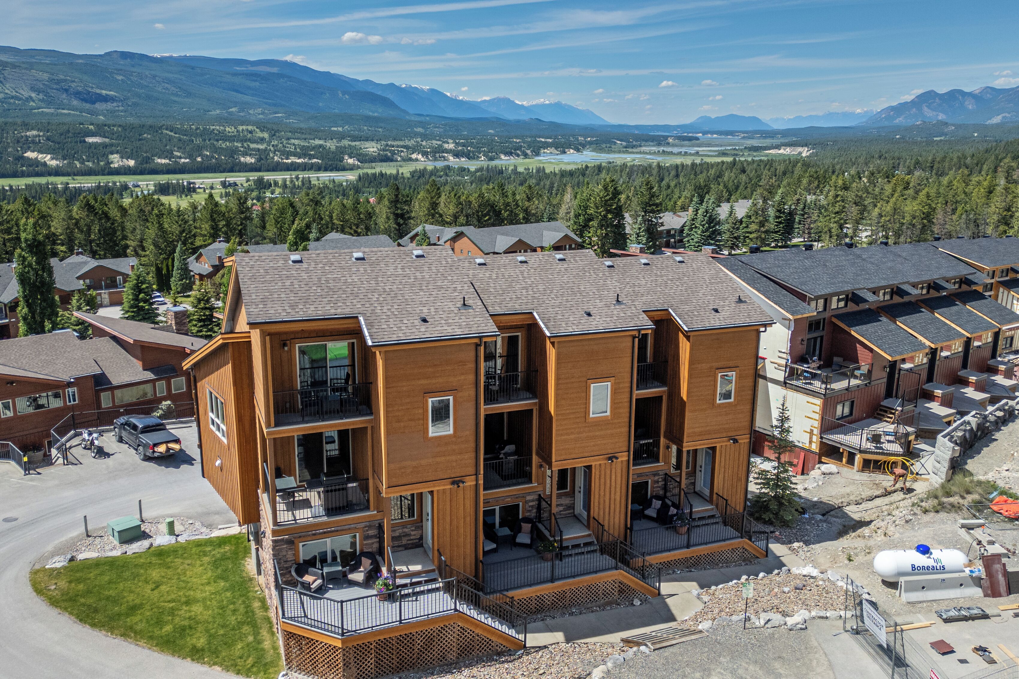 Un immeuble en bois à plusieurs étages, doté de balcons, d’un espace de stationnement et offrant une vue sur les montagnes et un lac.