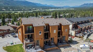 Un immeuble en bois à plusieurs étages, doté de balcons, d’un espace de stationnement et offrant une vue sur les montagnes et un lac.