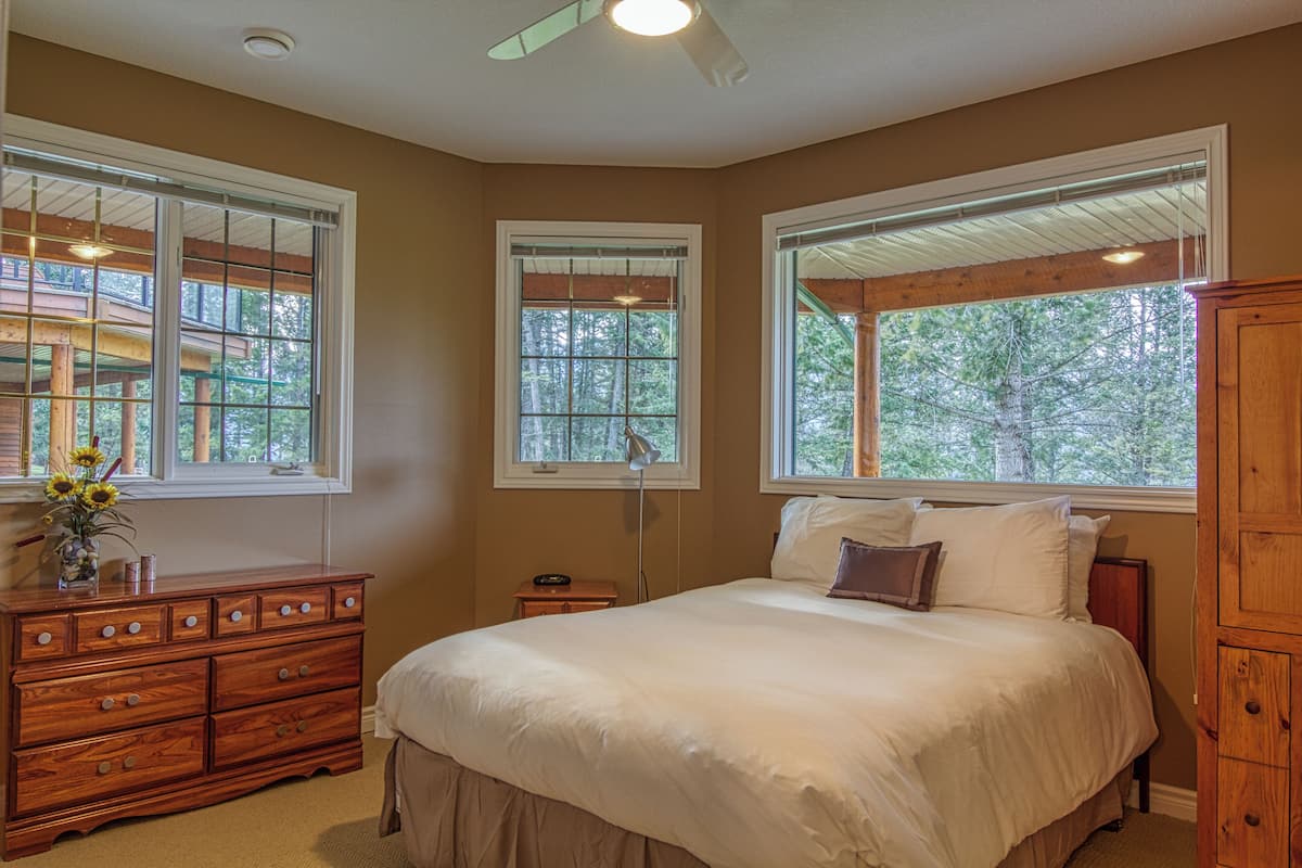 A bedroom with a large bed, two windows, a dresser, and a ceiling fan.