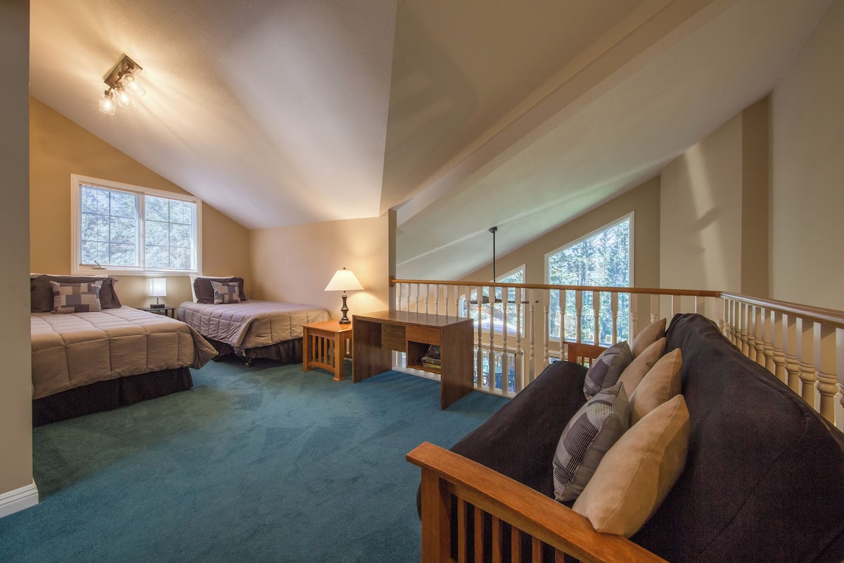 A bedroom with two beds, a desk, and a balcony with a railing.