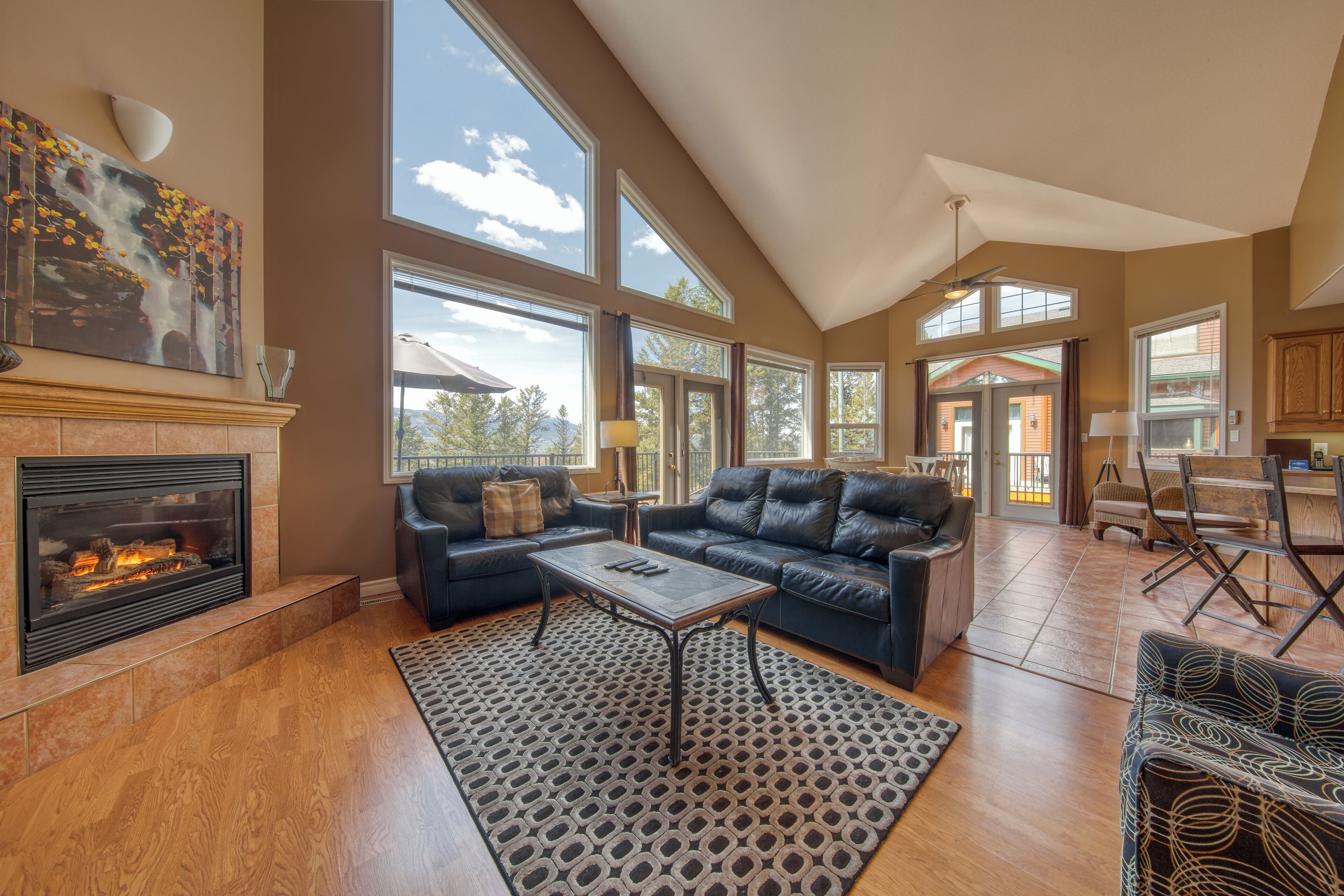A spacious living room with a fireplace, large windows, and a high ceiling.