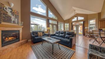A spacious living room with a fireplace, large windows, and a high ceiling.
