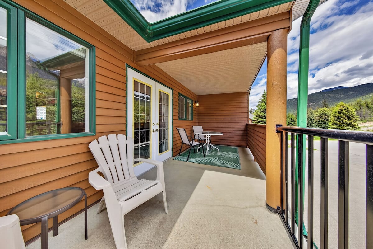 A wooden exterior with a covered porch, a white chair, a small table, and a view of mountains.