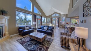A spacious living room with a fireplace, large windows, and a high ceiling.