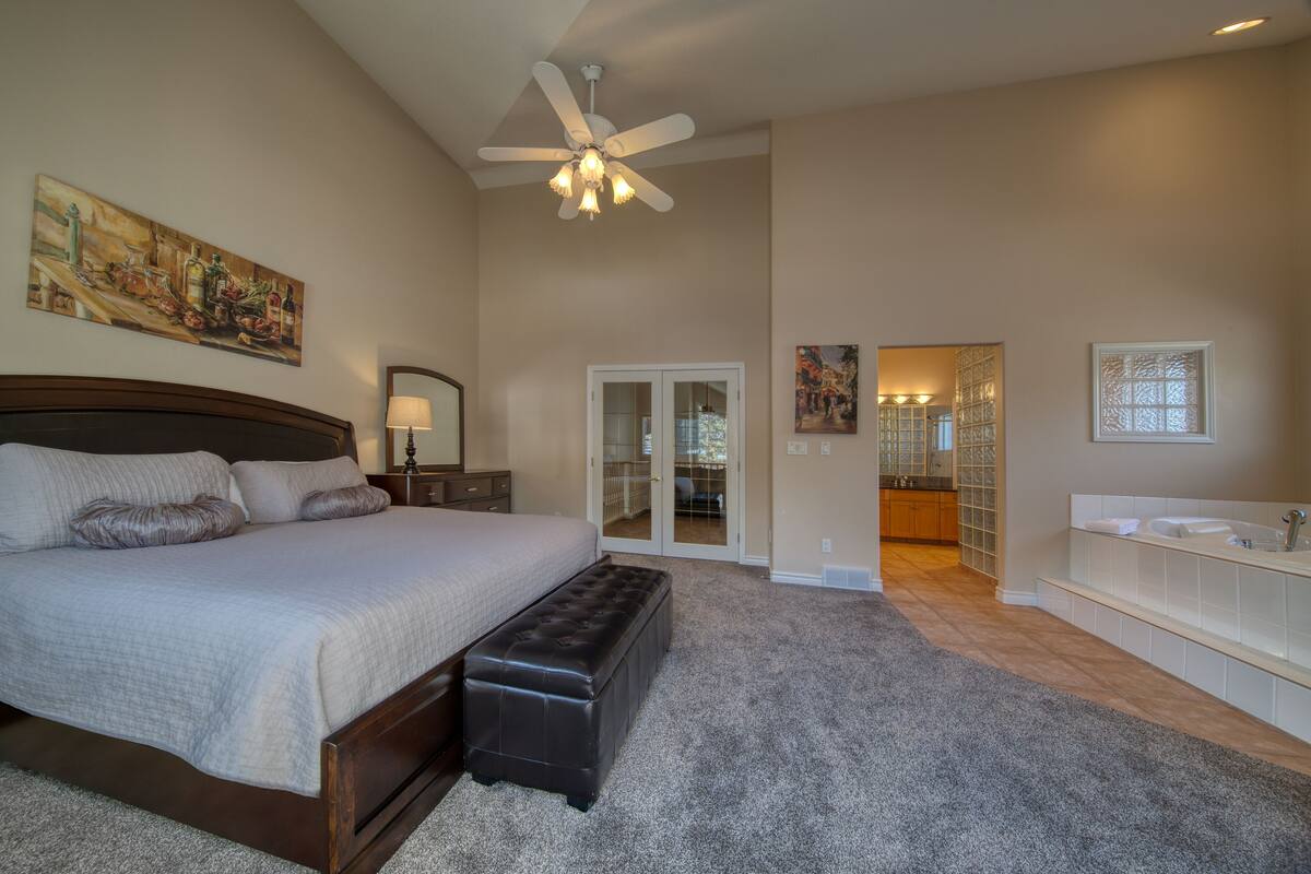 A bedroom with a bed, a bench, a ceiling fan, and a bathroom with a sink and mirror.