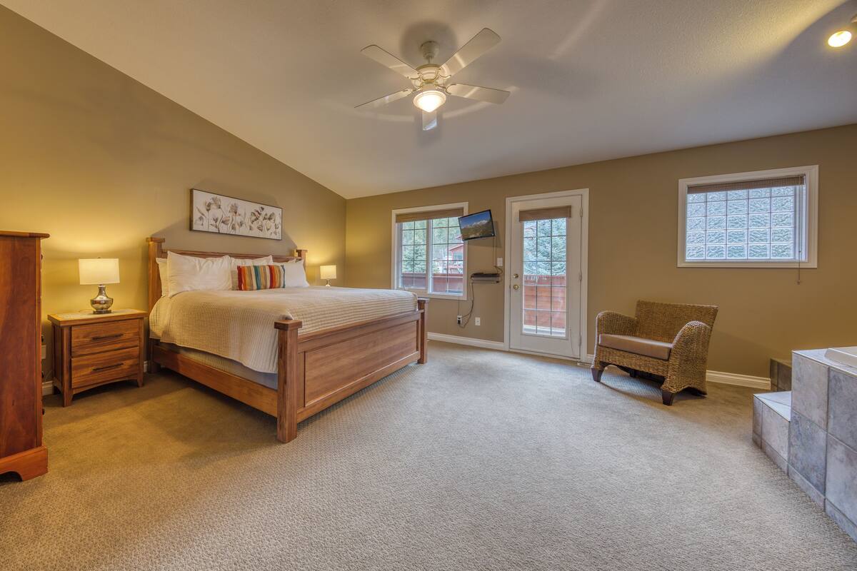 A bedroom with a bed, a nightstand, a chair, a ceiling fan, and a door with a view.