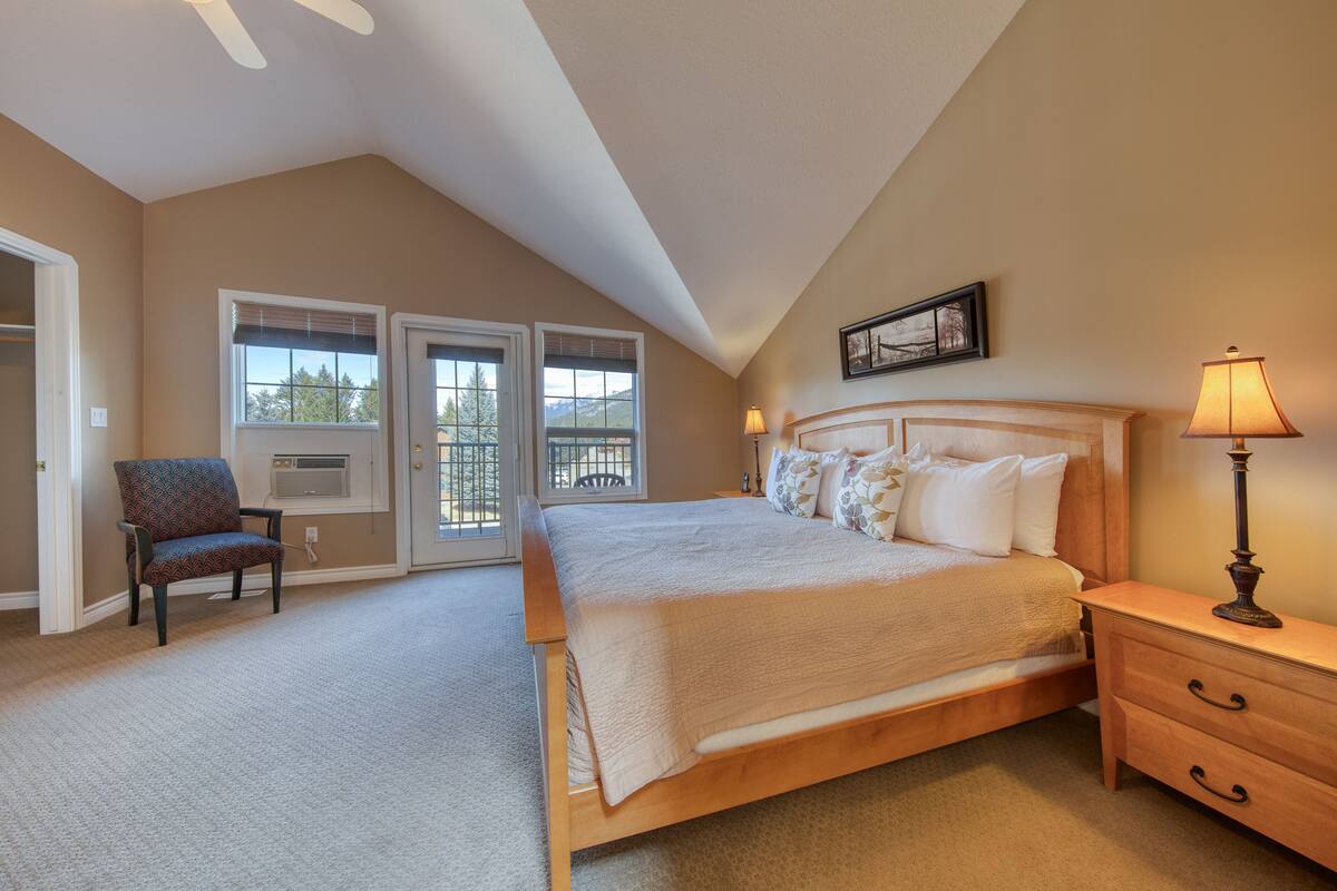 A bedroom with a large bed, a chair, a nightstand, and a window with blinds.