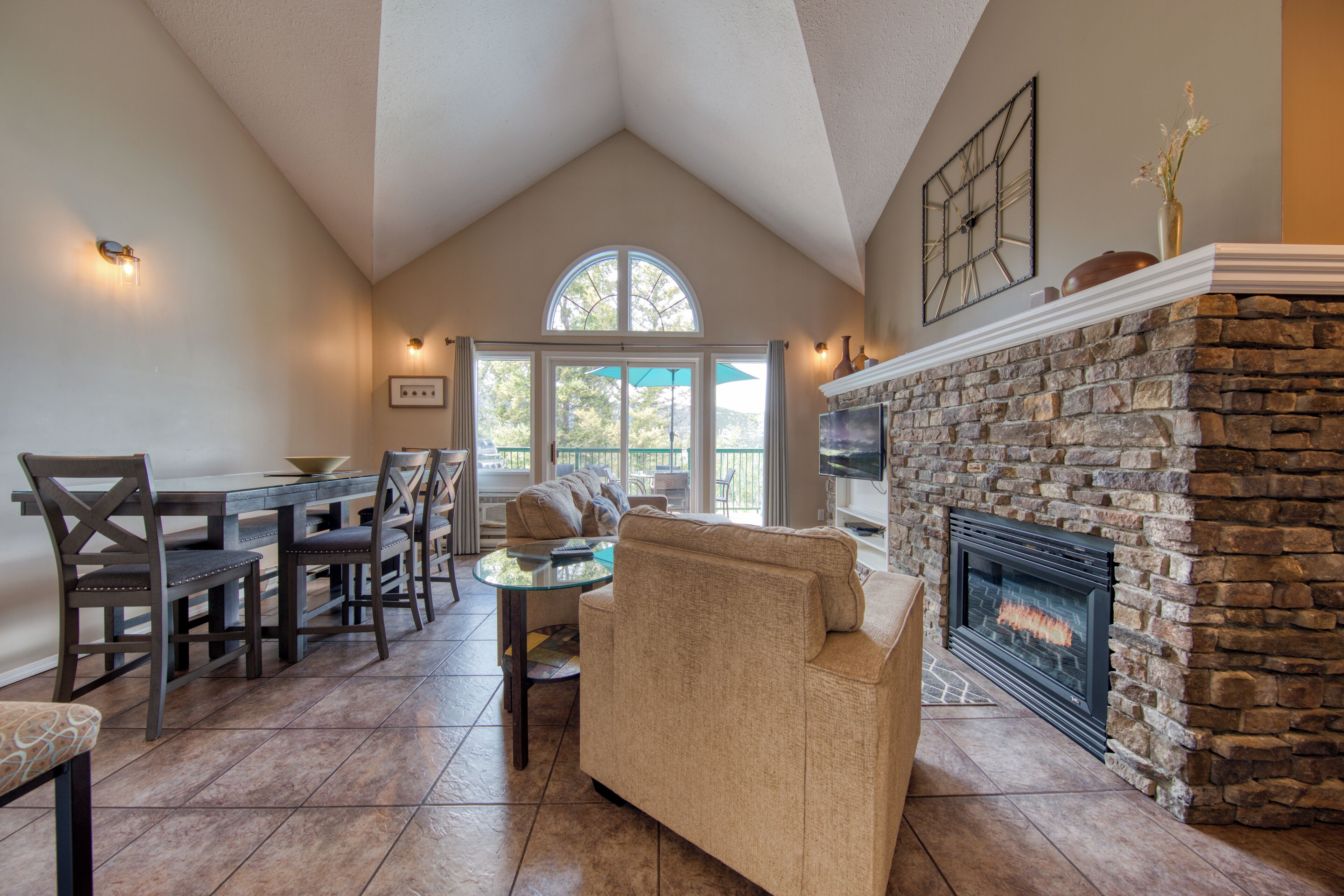 A cozy living room with a stone fireplace, a dining area with a table and chairs, and a large window with a view.