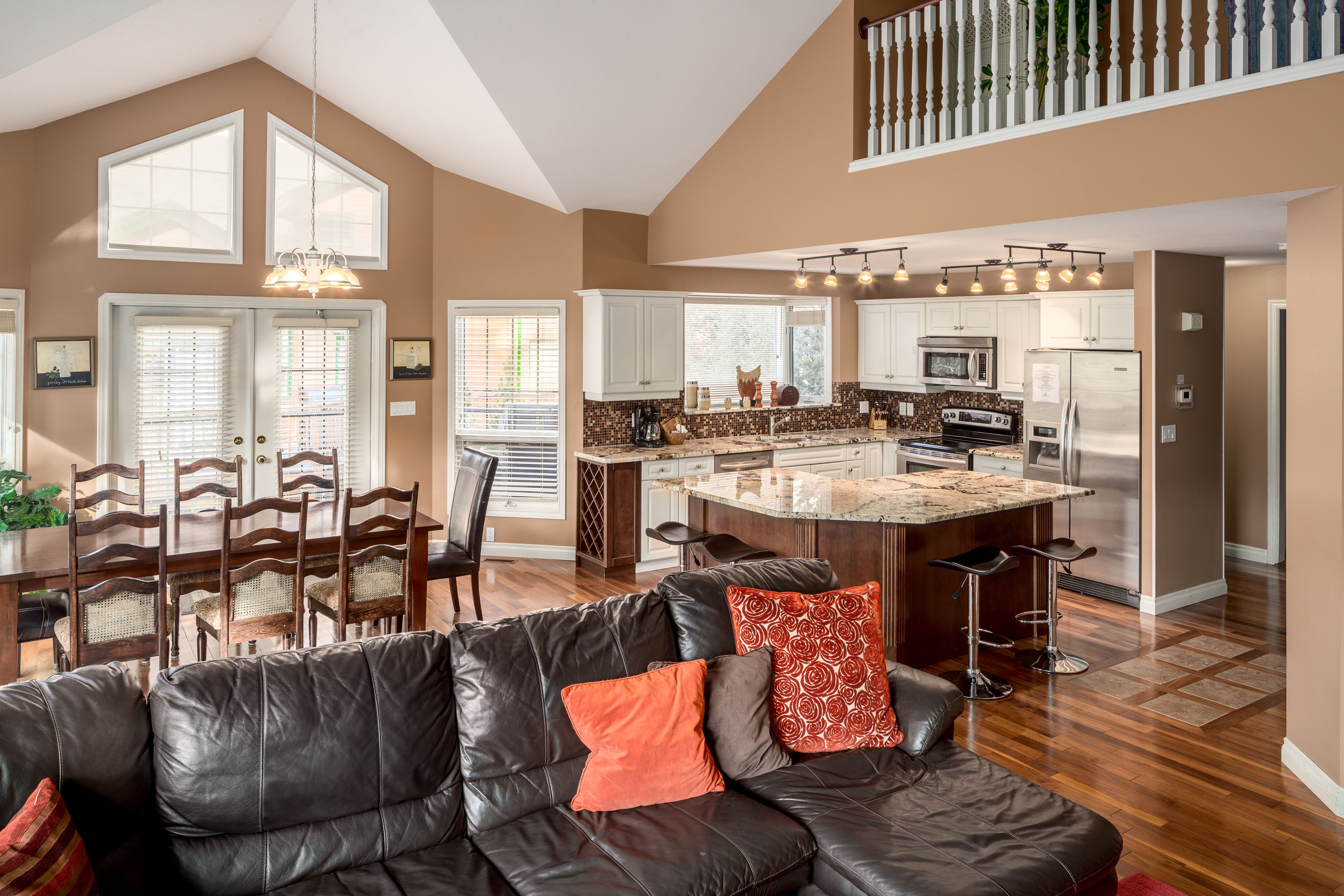 A spacious living area with a black leather sofa, a dining table with chairs, and a kitchen with a central island.