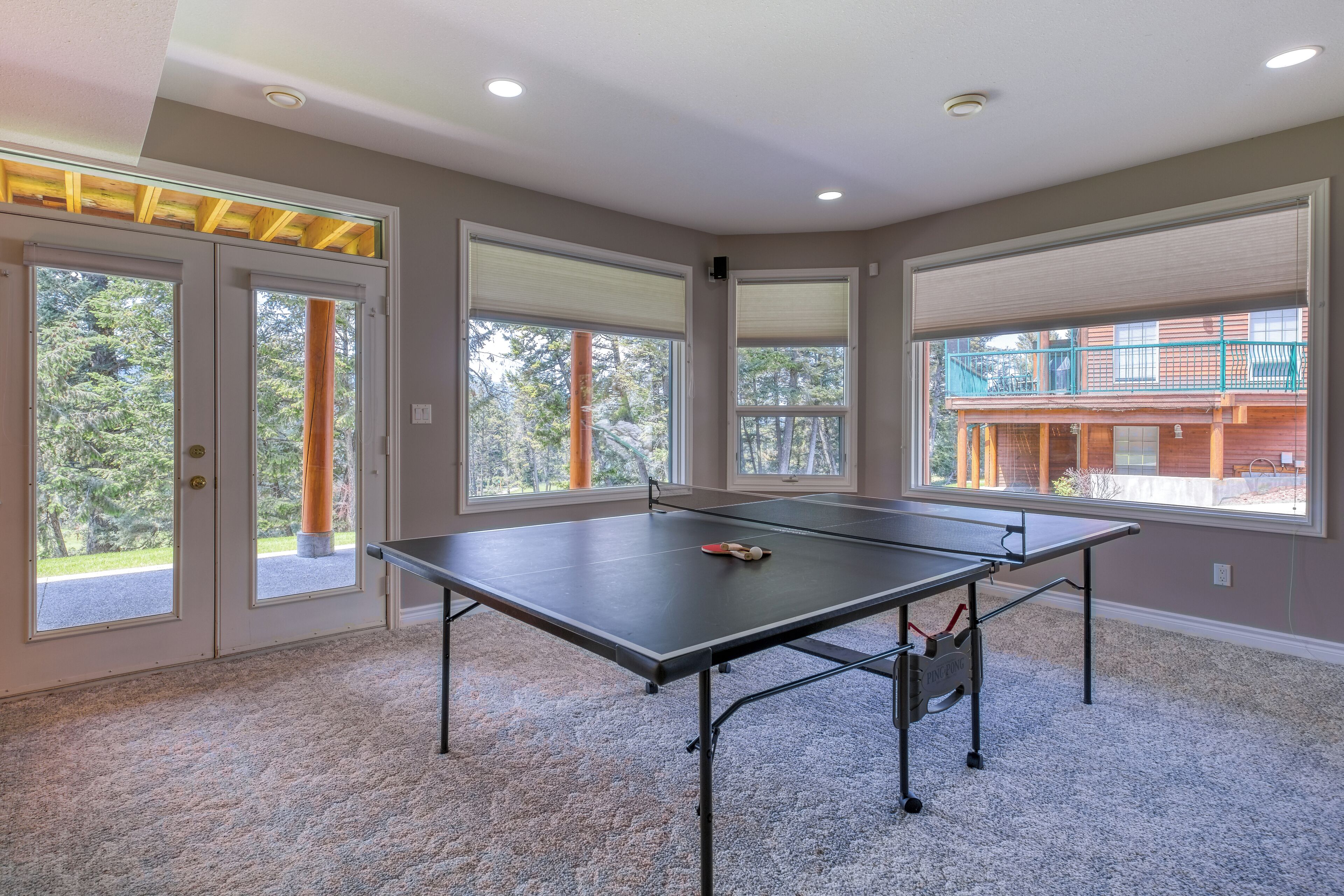 A ping pong table in a room with large windows and a view of a building outside.