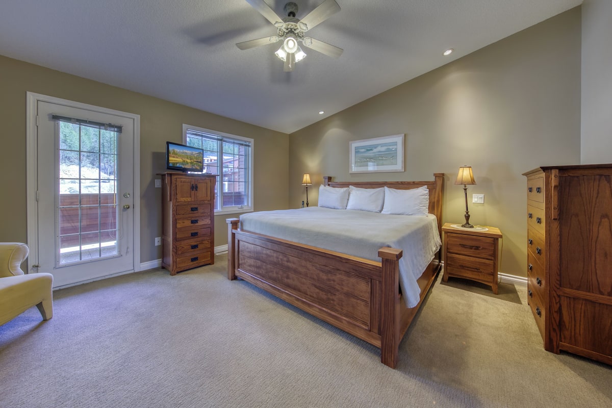 A bedroom with a bed, a ceiling fan, a TV, a dresser, and a window.