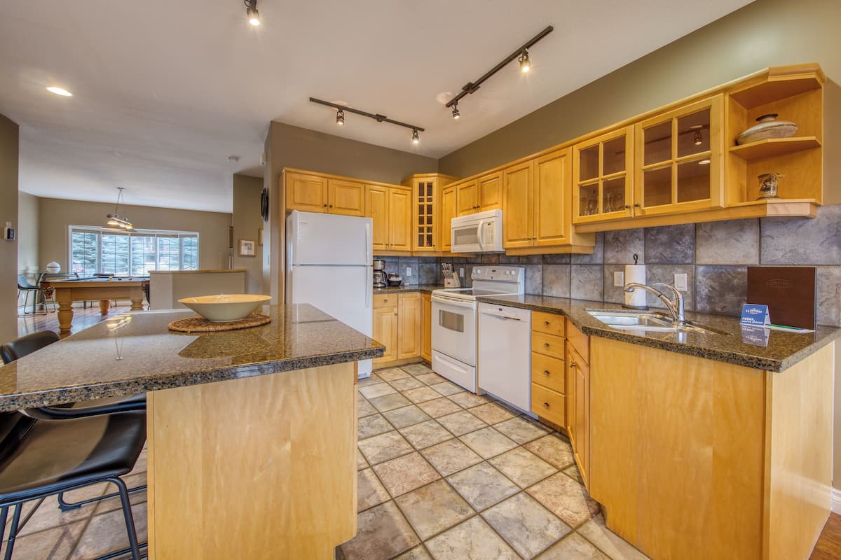 A kitchen with granite countertops, wooden cabinets, a refrigerator, stove, microwave, and a sink.