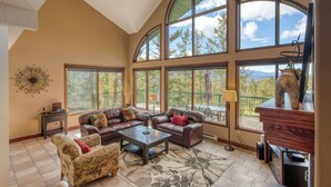 A spacious living room with leather sofas, a coffee table, and large windows offering a view of the outdoors.