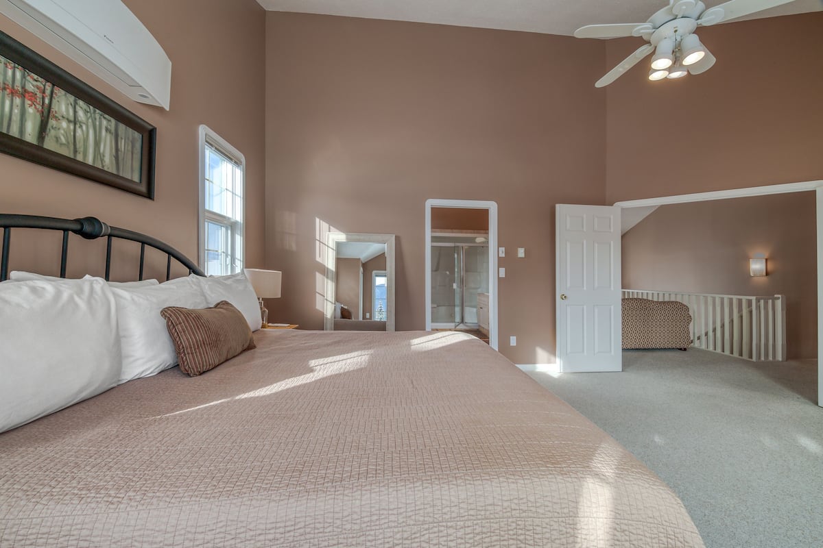A bedroom with a large bed, a ceiling fan, a window, and a door leading to another room.