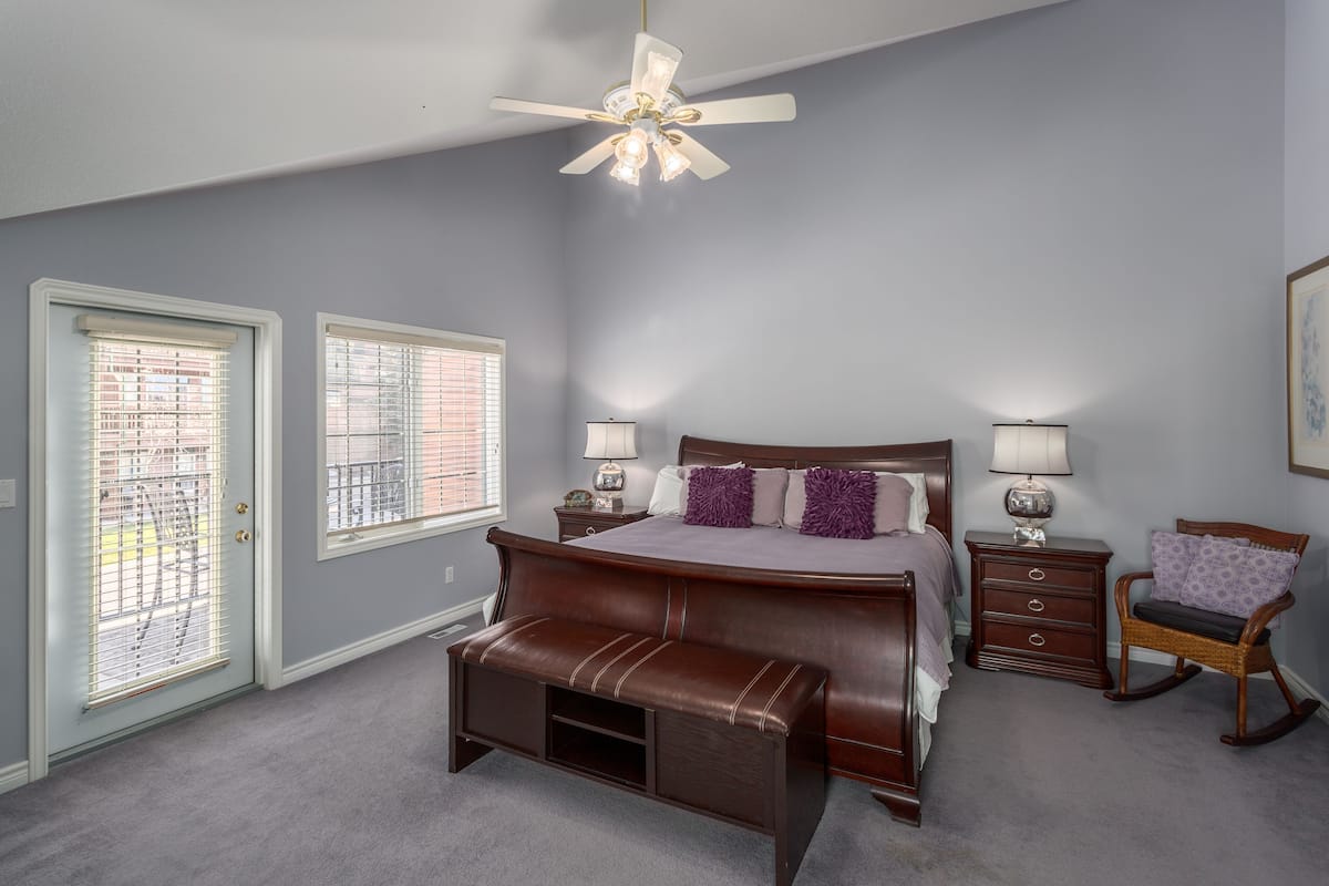 A bedroom with a bed, two bedside tables, a bench, a rocking chair, and a ceiling fan.