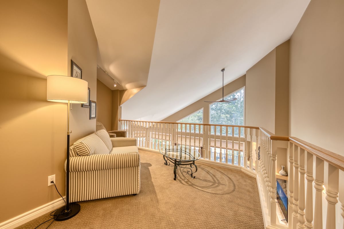 A spacious balcony with a high ceiling, a cushioned seating area, and a glass table.