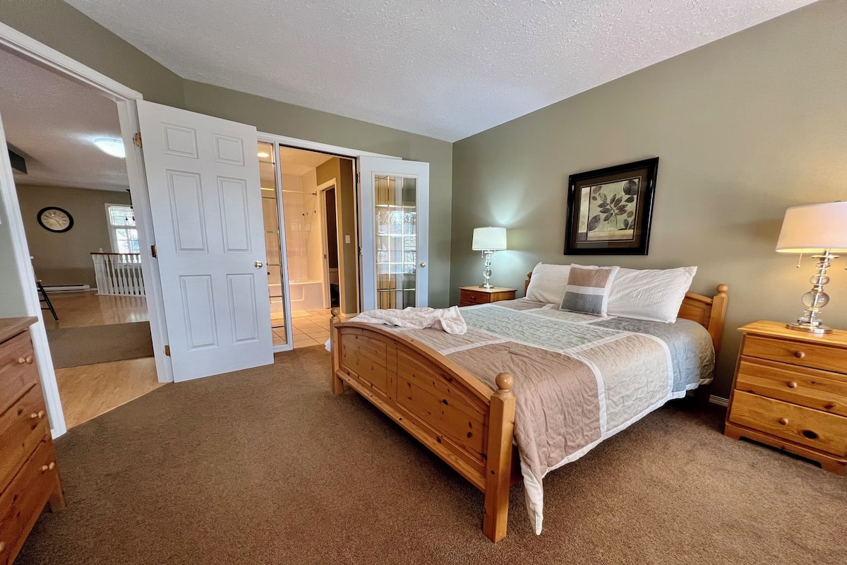 A bedroom with a wooden bed, a nightstand, a dresser, and a door leading to a bathroom.