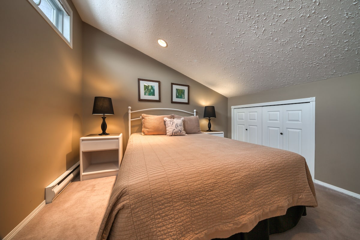 A bedroom with a bed, nightstands, a window, and a door.