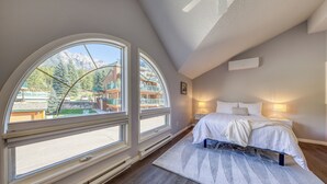 A bedroom with a large window, a bed, and a nightstand.