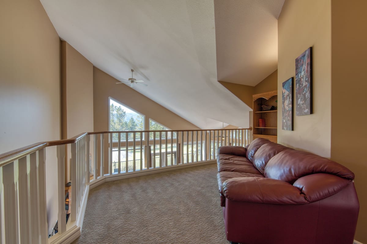 A spacious room with a high ceiling, a brown leather sofa, a white railing, and a view of the outdoors.