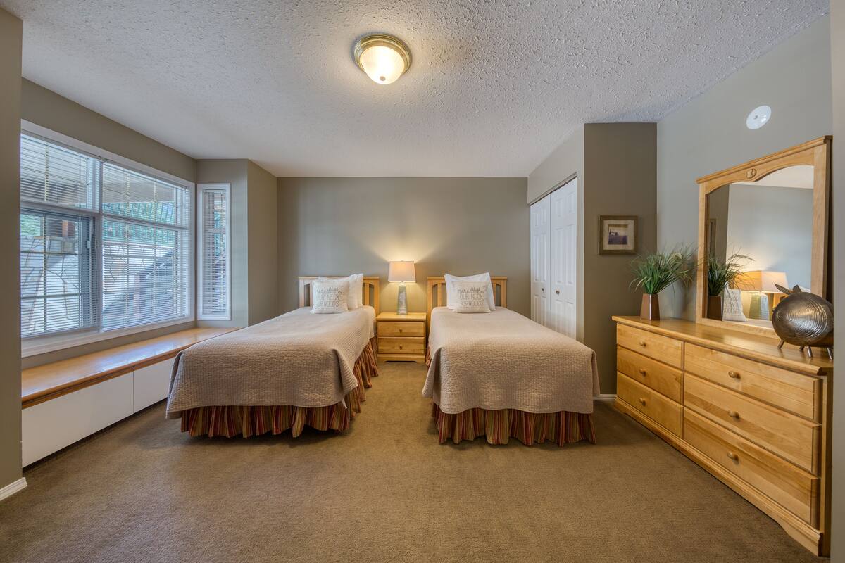 A bedroom with two beds, a dresser, a nightstand, and a window with blinds.