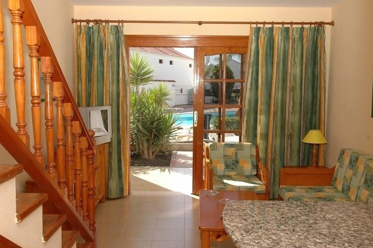 Una stanza con un letto, un tavolino, una sedia, una scala in legno e vista su un'area piscina.