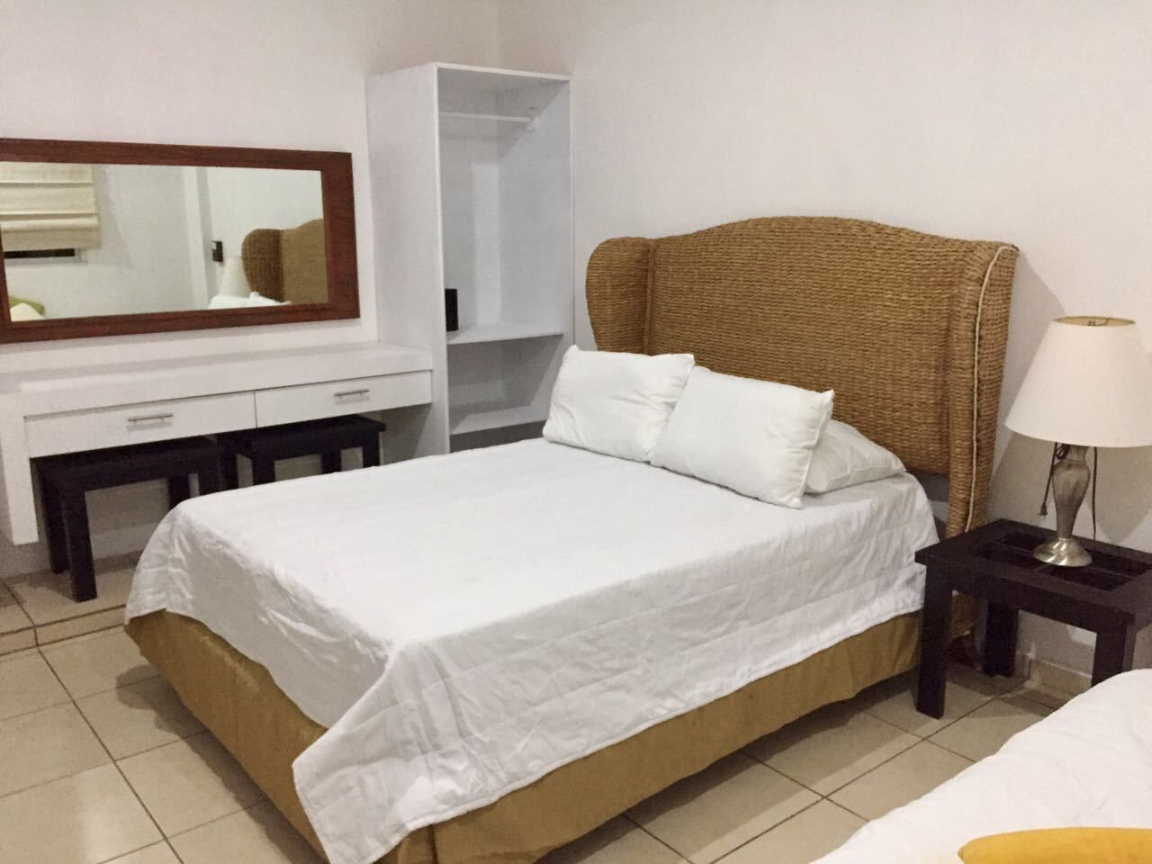 A hotel room with a bed, a desk, a wardrobe, and a nightstand with a lamp.