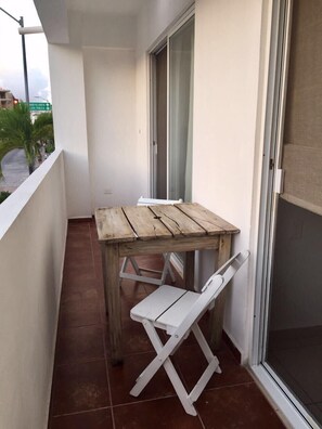 A balcony with a wooden table and a white folding chair.