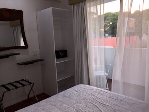 A bedroom with a bed, a wardrobe, a mirror, and a window with sheer curtains.