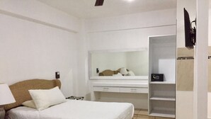 Una camera d'albergo con un letto, un comodino, una lampada, una cassettiera, uno specchio e un armadio.