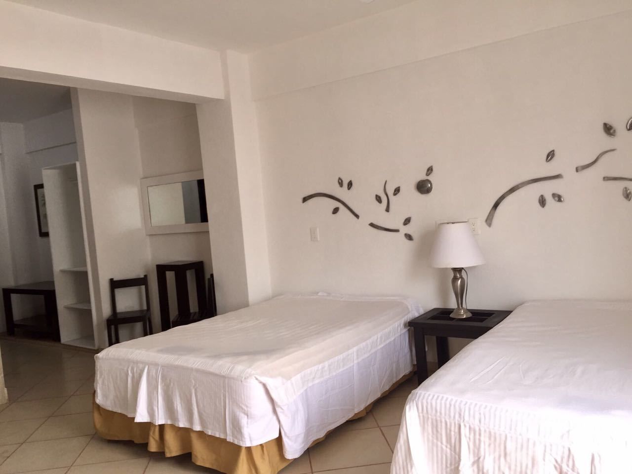 Una habitación de hotel con dos camas individuales, una mesita con una lámpara, una silla y un espejo en la pared.