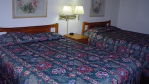 Ein Zimmer mit zwei Betten, jeweils mit blumigem Bettzeug, einem Nachttisch mit Lampe sowie zwei gerahmten Blumenbildern an der Wand.