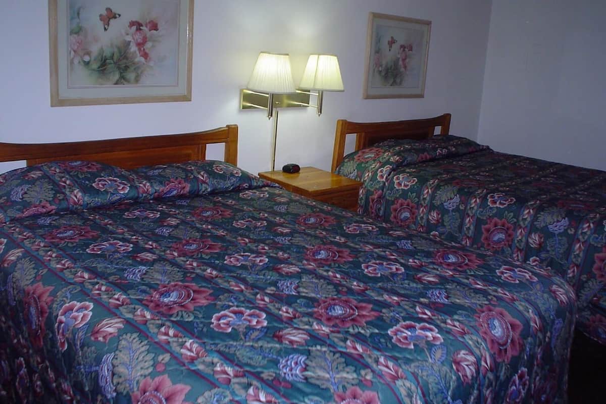 A room with two beds, each with floral-patterned bedding, a bedside table with a lamp, and two framed floral paintings on the wall.