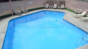 Ein Pool mit gewölbter Kante, umgeben von einem weißen Zaun und mehreren Liegestühlen.