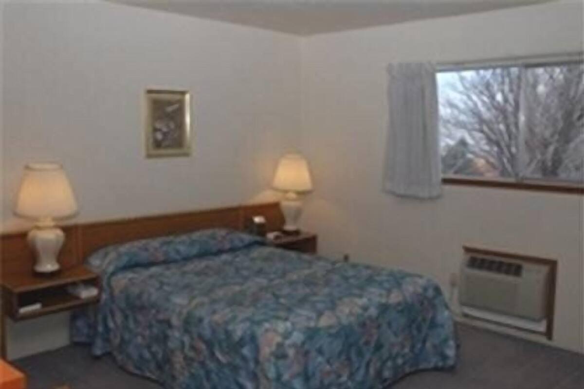 A hotel room with two beds, each with a matching nightstand and lamp, a framed picture on the wall, and a window with curtains.