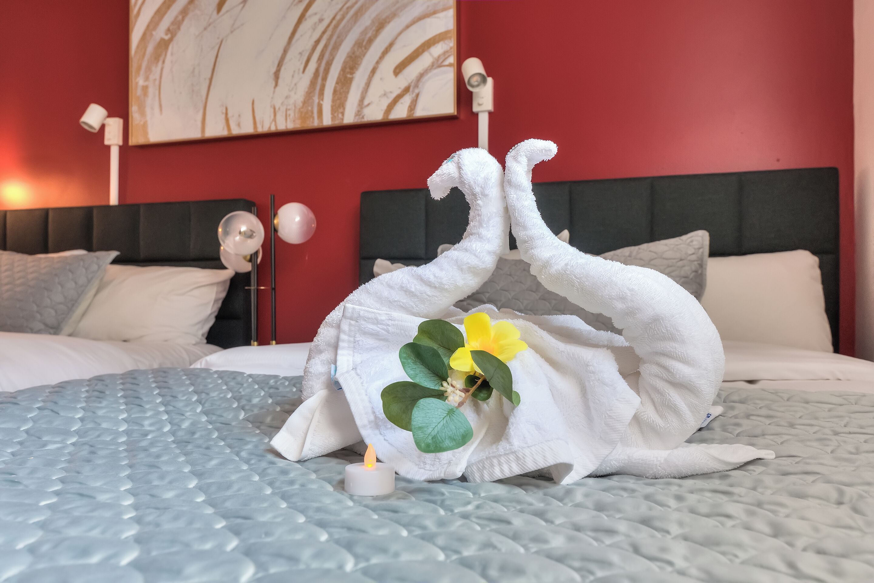 Una cama con una escultura de toalla blanca, una vela pequeña y una planta decorativa.