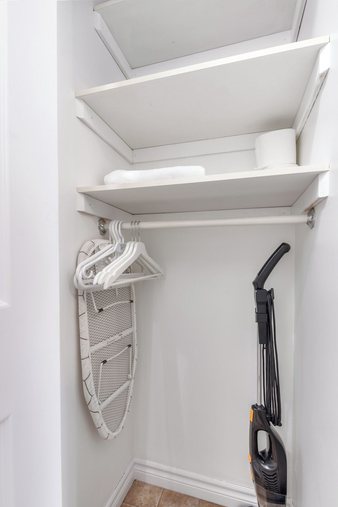 Un armario con estantes blancos, una barra para colgar y un aspirador.