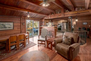 Interior de uma cabana de madeira com sala de jantar, sala de estar com sofá e poltrona, cozinha e escada.