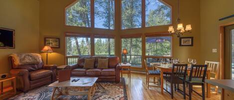 A spacious living room with a large window, a fireplace, a dining area, and a cozy seating area.