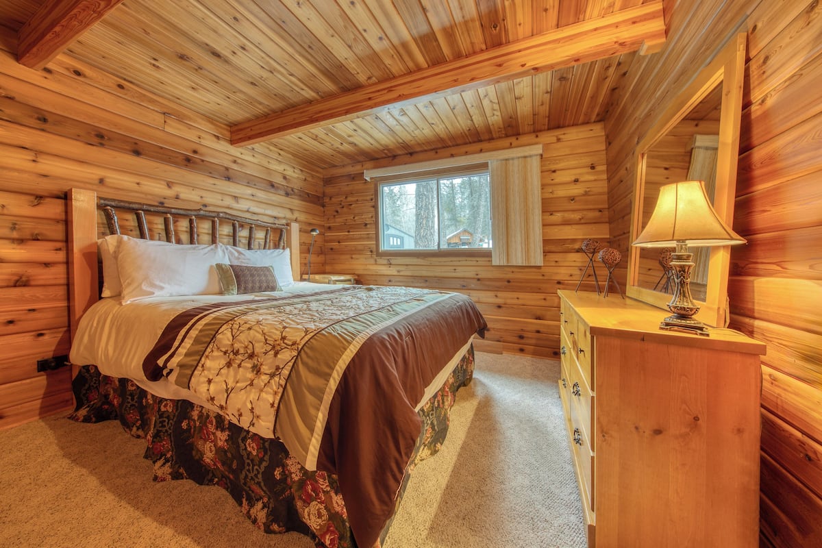 Un dormitorio de cabaña de madera con una cama, cómoda y ventana.