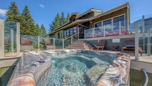 Un jacuzzi con cerramiento de vidrio, terraza de madera y zona de estar al aire libre con sillas y una mesa.