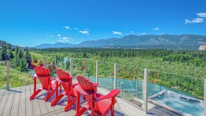 Terraza con sillas rojas que da a un jacuzzi y una vista panorámica de un río y montañas.