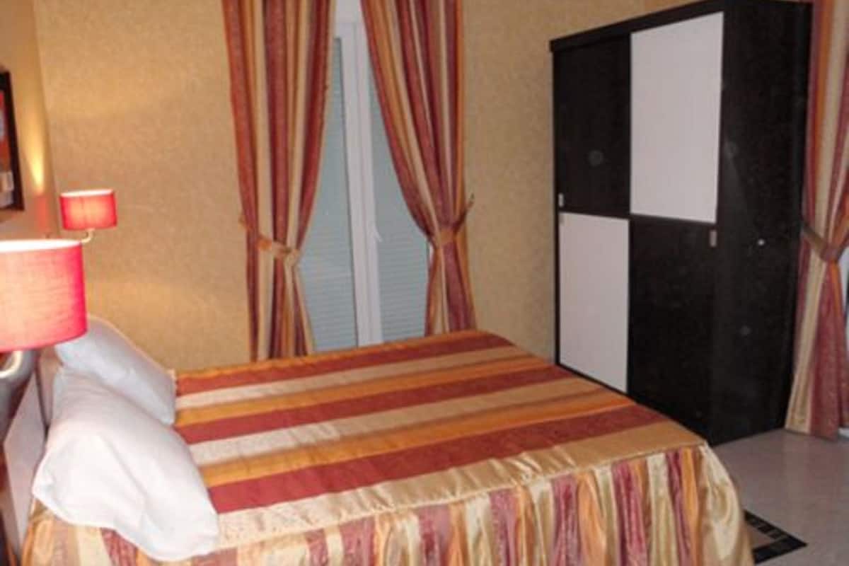 A hotel room with a bed, a wardrobe, and curtains.