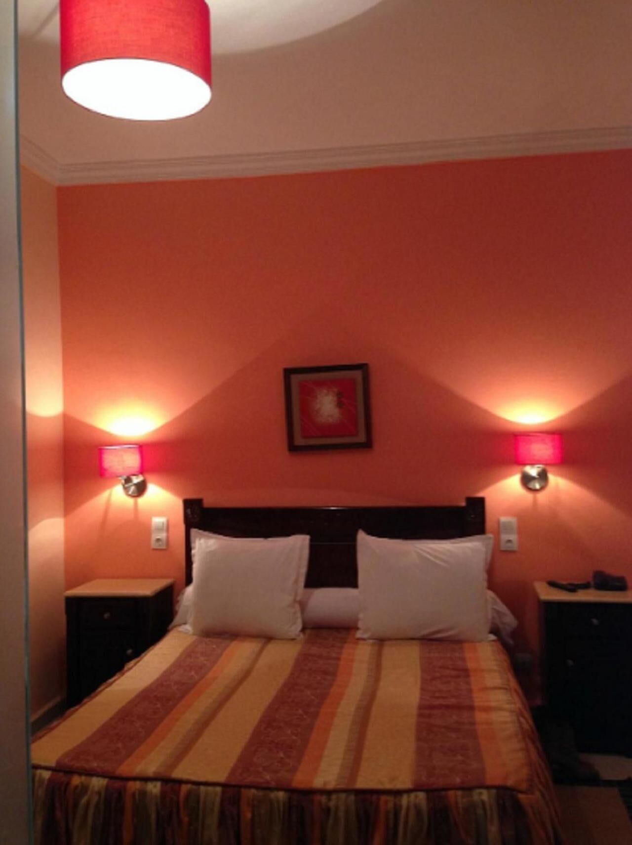 A hotel room with a bed, two bedside lamps, and a framed picture on the wall.