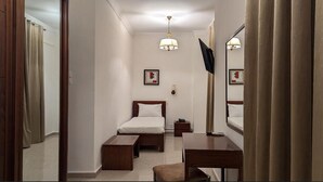 A hotel room with a bed, bedside table, a desk with a chair, a mirror, a TV, and a framed picture on the wall. -  Hôtel Audin (Algiers)