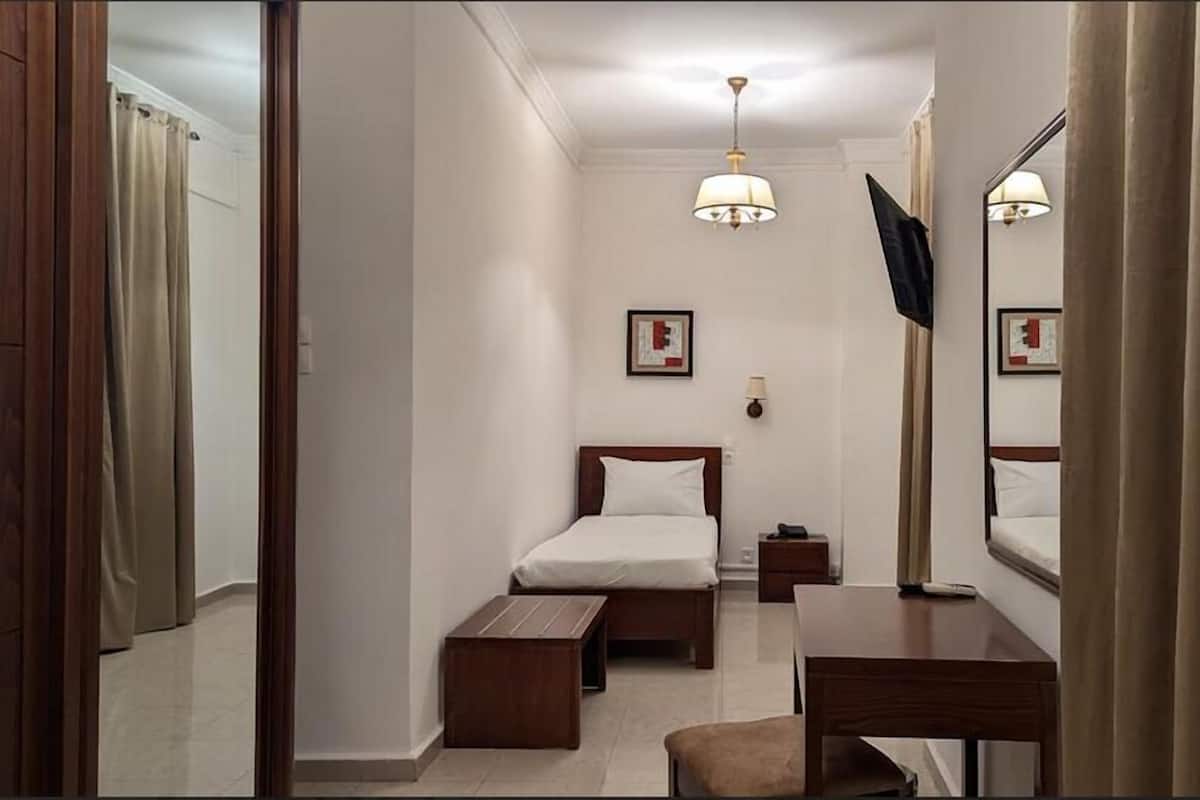 A hotel room with a bed, bedside table, a desk with a chair, a mirror, a TV, and a framed picture on the wall.