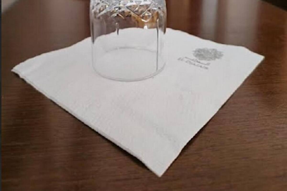 A clear glass tumbler on a white napkin on a wooden table.