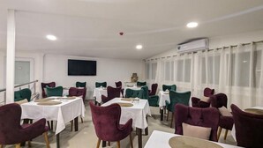 A conference room with multiple tables and chairs, a mounted television, and a large window with curtains. -  Hôtel Audin (Algiers)